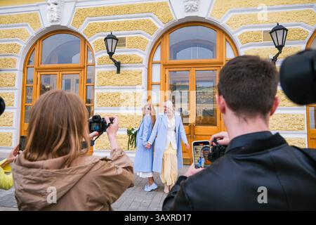 Moskau, Russland, 31.03.2025 Ein Mann und eine Frau fotografieren eine Frau in einem gelben Kleid. Die Frau trägt einen blauen Mantel und ein weißes Hemd Stockfoto