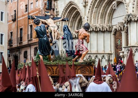 Der Paso "La Exaltación" der ehrwürdigen Hermandad del Santísimo Cristo del Perdón steht vor dem gotischen Portal der Kathedrale von Cuenca, Castilla-La Mancha, Spanien. Zwei Soldaten heben die von Luis Marco Pérez 1951 geschaffene Christusfigur auf das Kreuz. Der Bau der Kathedrale von Santa María y San Julián begann 1182 und sie wurde 1208 geweiht, was sie in ihrem französisch beeinflussten gotischen Stil zu einem der frühesten gotischen Gebäude des Landes macht. Die heutige Fassade wurde nach einem teilweisen Einsturz 1902 im neugotischen Stil wiederaufgebaut. Während der Semana Santa in Cuenca nehmen 33 Hermandades teil Stockfoto