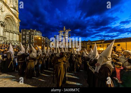 Reihen von Mitgliedern der Hermandad de la Cruz Desnuda de Jerusalén, in braunen und weißen Gewändern, säumen die Plaza Mayor in Cuenca, während das Kreuz an der Kathedrale vorbeigetragen wird. Kastilien-La Mancha, Spanien. Während der Semana Santa ziehen 33 Hermandades durch die Straßen von Cuenca und nehmen an insgesamt elf Prozessionen während der Heiligen Woche teil. Die Abendprozession am Karfreitag, die um 21 Uhr in der Kathedrale von Cuenca beginnt, ist geprägt von einem besonderen Gefühl der Feierlichkeit, Stille und einer beeindruckenden Atmosphäre Stockfoto