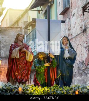 Statuen von Maria, Martha und Magdalena mit einem großen Holzkreuz mit weißem Schleier während einer Prozession durch die engen Gassen einer historischen Stadt in Süditalien Stockfoto