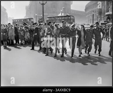 VJ DAY LONDON britische Zivilisten und Servicemitarbeiter im Londoner Piccadilly Circus feiern die Nachricht vom Sieg der Alliierten über Japan im August 1945. DAS ENDE DES Zweiten Weltkriegs im Londoner Piccadilly Circus, eine Gruppe von Soldaten und Frauen, verbindet ihre Arme, während sie zur Kamera gehen, singen und tanzen, um Eros zu feiern, um die Nachricht zu hören, dass der Krieg in Japan vorbei ist. Hinter ihnen versammeln sich Menschenmassen im Sonnenschein. Mehrere Busse sind ebenfalls zu sehen. Blick von der Eros-Statue in Richtung Piccadilly & Regent Street. London UK Datum 1945 Stockfoto