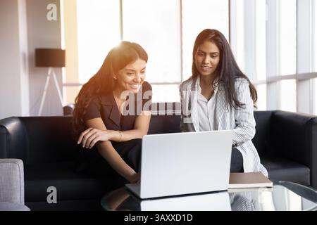 Zwei Frauen, die einen Laptop auf der Couch in der Lobby des Büros benutzen Stockfoto