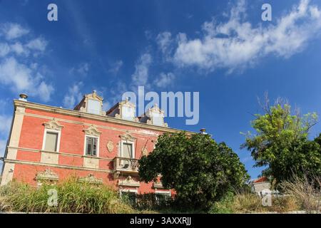 Ein altes Backsteingebäude mit detaillierten Fensterrahmen und verzierten Zierleisten, umgeben von einer alten Steinmauer und bewachsenen Pflanzen. Die ruhige Atmosphäre ist s Stockfoto