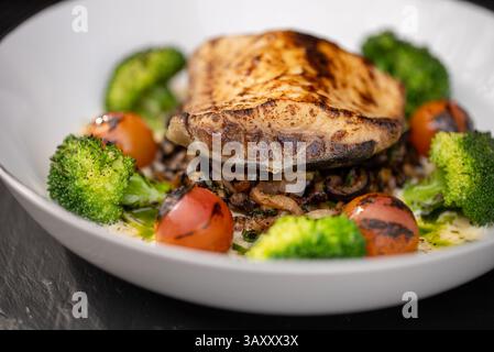 Gegrillter Weißfisch auf sautiertem Pilzzwiebelmedley, mit verkohlten Kirschtomaten und gedämpften Brokkoli-Röschen für ausgewogene Ergebnisse Stockfoto