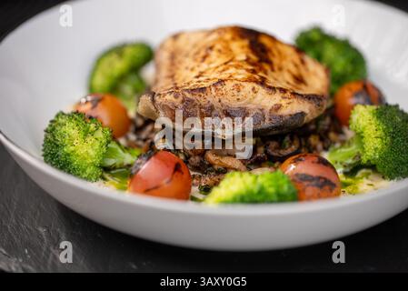 Gegrillter Weißfisch auf sautiertem Pilzzwiebelmedley, begleitet von blanchiertem Brokkoli und verkohlten Kirschtomaten, die nahrhaft sind Stockfoto
