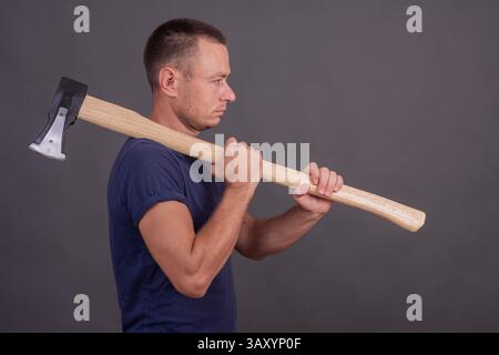 Ein Mann mit einer Axt auf grauem Hintergrund. Seitenansicht Stockfoto