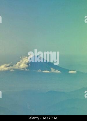 Mount Fuji über Wolkenschicht auftaucht - majestätischer Vulkan erhebt sich über Wolken und enthüllt die raue Schönheit der Natur bei Sonnenaufgang mit leuchtenden Farben am Himmel ( Luftlandschaftsfoto ) Stockfoto