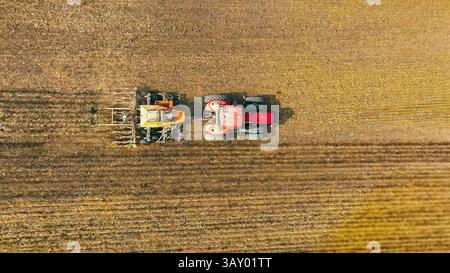 Luftaufnahme des Pflugfeldes des des Traktors. Ansicht von oben auf einen roten Traktor mit landwirtschaftlichen Geräten, der während der Herbstlandung ein großes braunes Feld bewirtschaftet Stockfoto