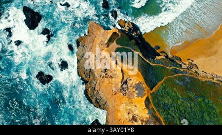 Blick aus der Vogelperspektive auf die Küstenklippen und das Meer. Drohnenaufnahme von dramatischen Küstenklippen, umgeben von türkisfarbenen Meereswellen und Sandstränden, zeigt Stockfoto