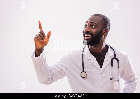 Porträt eines männlichen Afroamerikaners, der eine Idee hat und auf dem grauen Hintergrund nach oben zeigt. Stockfoto