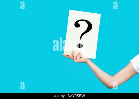 Hand mit weißem Fragezeichen vor blauem Hintergrund. Fragezeichensymbol. Leerzeichen für Text. Hand hält Papier ein Fragezeichen. Weiblich Stockfoto