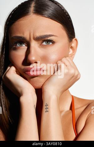 Eine hübsche junge Frau mit Sonnenbräune sieht nachdenklich aus und schützt ihr Gesicht vor Sonnenlicht. Stockfoto
