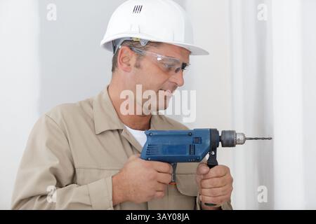 Mitte der erwachsene Mann bohren Loch in Wand Stockfoto