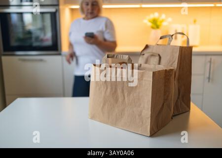 Seniorin, die Lebensmittel erhält, Einkaufstaschen auf dem Tisch in der Küche Stockfoto