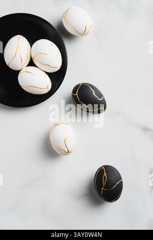 Weiße und schwarze Ostereier verziert Gold auf Marmortisch. Flach liegend, Draufsicht. Frohe Ostern Karte. Stockfoto