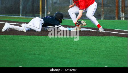 High School Baseballspieler taucht zurück zur ersten Basis auf einem Pick-off-Versuch während eines Spiels. Stockfoto