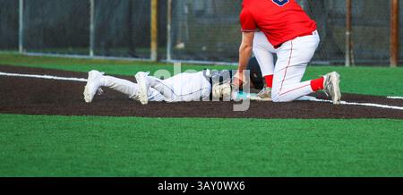 Der erste Baseman, der das Schild auf einem Läufer platziert, der während eines High School Baseballspiels zurück zur Basis taucht. Stockfoto