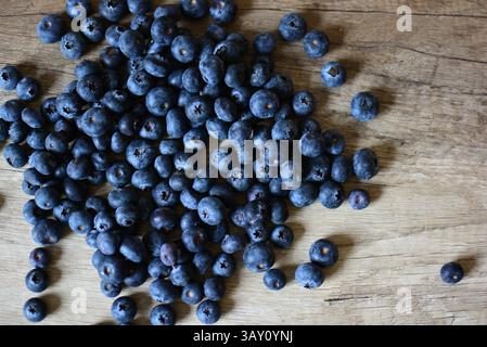 Frische Heidelbeeren auf Holztisch mit Blick auf die Tischplatte. Viele blaue Beeren fallen auf Holztisch. Stockfoto