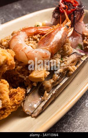 Auf der verführerischen Platte mit Meeresfrüchten werden gegrillte Muscheln, gebratenes Huhn und saftige Garnelen mit Reis und frischem Ceviche serviert Stockfoto