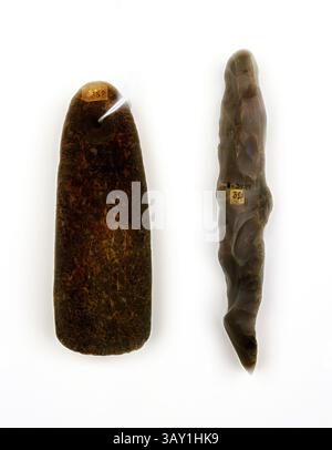 Zwei Artefakte aus Stein werden nebeneinander angezeigt. Das linke Teil ist flach und rechteckig mit einer glatteren Oberfläche und einem eindeutigen Etikett. Das richtige Stück hat eine länger gestreckte und kurvigere Form, die eine rauere Textur und ein weiteres Etikett aufweist. Beide zeigen komplizierte natürliche Muster und Farbvarianten, die auf ihre historische Bedeutung und Handwerkskunst hinweisen. Europäisch, Kelt und Meißel, kein Datum, Stein, insgesamt (celt): 12,7 x 4,1 x 2,5 cm (5 x 1 5/8 x 1 Zoll), klassische Kunst mit einem modernen Twist, der von Artotop neu interpretiert wurde Stockfoto
