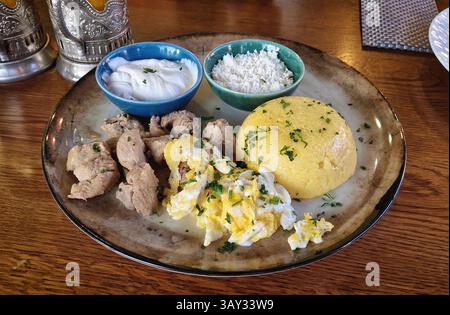 Traditionelles moldauisches Essen, Nahaufnahme mit Schweineeintopf, Mamaliga Polenta, Spiegeleiern, Käse und Sauerrahm mit Petersilie Stockfoto