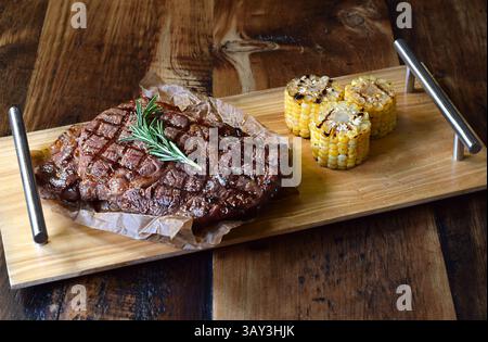 Gegrilltes Rindersteak auf Holzbrett mit gegrilltem Mais Stockfoto