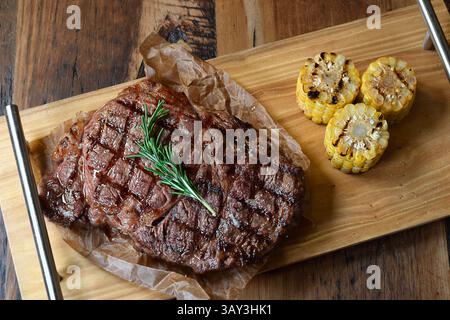 Gegrilltes Rindersteak von oben auf Holzbrett mit gegrilltem Mais garniert mit Rosmarinzweig Stockfoto