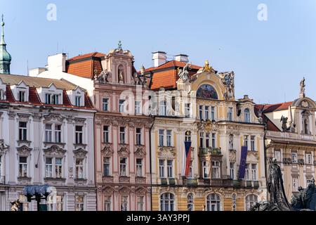 A die komplizierten Fassaden und roten Dächer alter Prager Gebäude unter einem klaren blauen Himmel. Architektonische Details, Statuen und farbenfrohe Stuckarbeiten Stockfoto
