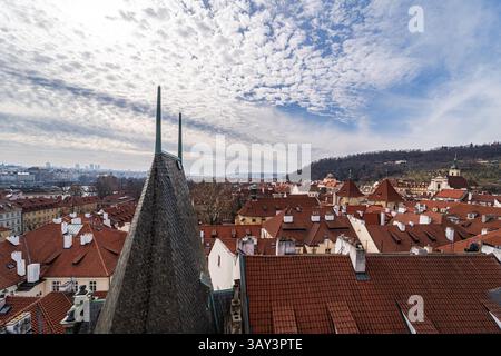 Fesselnde Luftaufnahme mit den geschäftigen Dächern von Prag, hervorgehoben durch eine malerische Kulisse aus üppigen Hügeln und strukturierten Wolken. Stockfoto