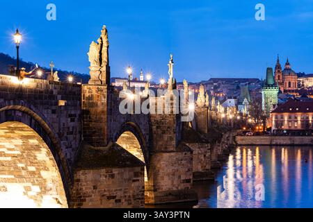 Atemberaubender Blick auf die Karlsbrücke in Prag mit Statuen und Stadtlichtern, die während der Dämmerung auf der Moldau reflektieren. Stockfoto