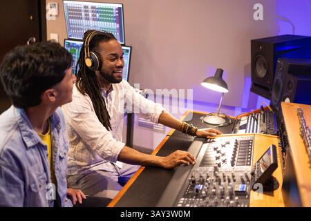 Zwei Toningenieure arbeiten in einem Aufnahmestudio mit Audiogeräten und Computerbildschirmen zusammen. Die moderne Einrichtung unterstreicht den Fokus und die Teamfähigkeit Stockfoto