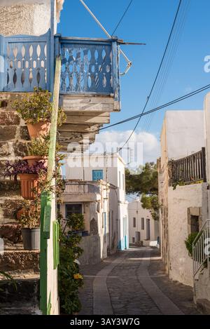 Sonnenbeschienene Gasse in Trypiti mit weiß getünchten Gebäuden mit blauen Akzenten, Topfpflanzen und einem ruhigen Himmel. Eine typisch griechische Inselszene auf Mi Stockfoto