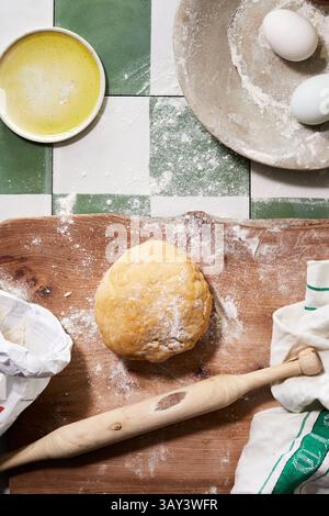 Blick von oben auf eine rustikale Kücheneinrichtung für hausgemachte Pasta und Gebäck, mit einer gut gekneteten Teigkugel auf einem bemehlten Holzbrett, einer Nudelnadel, Stockfoto