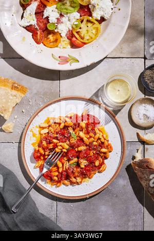 Blick von oben auf eine hausgemachte Mahlzeit mit frisch zubereiteten Nudeln, die mit einer reichhaltigen Tomatensauce überzogen sind, ergänzt durch einen bunten Tomatensalat mit abwechslungsreichen Erbstücken Stockfoto