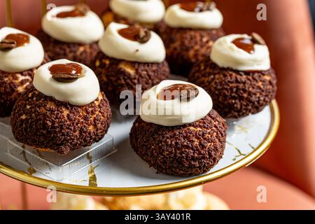 Genießen Sie diese exquisiten Kaffeespezialitäten mit üppiger Creme und einer Beilage aus Kaffeebohnen, die elegant auf einem goldenen Kuchenständer präsentiert werden. Stockfoto