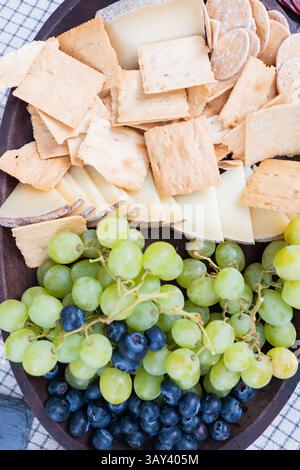 Eine Nahaufnahme einer gemischten Käseplatte mit verschiedenen Crackern, grünen Trauben und Heidelbeeren. Perfekt für gesellschaftliche Zusammenkünfte, Partys oder als A Stockfoto