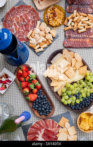 Eine einladende Wurstplatte umfasst verschiedene Käsesorten, Wurstwaren, Cracker, frische Erdbeeren, Heidelbeeren, und Trauben, ideal für ein gemütliches Treffen Stockfoto