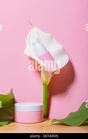Elegantes Kosmetikglas mit einer lebendigen Calla-Lilie auf rosa Hintergrund, die auf Luxus und natürliche Schönheitspflege hindeutet. Stockfoto