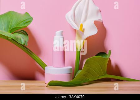 Rosafarbene Kosmetikprodukte mit üppig grünen Blättern und einer weißen Calla-Lilie vor einem leuchtend rosa Hintergrund, die ein erfrischendes, na präsentieren Stockfoto