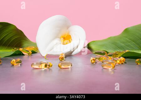 Ruhige Präsentation mit goldenen Omega-3-Öl-Ergänzungskapseln, eingebettet in eine weiße Calla-Lilie, umgeben von üppigen grünen Blättern gegen einen weichen rosa bac Stockfoto