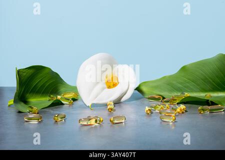 Ruhige Präsentation mit goldenen Omega-3-Öl-Ergänzungskapseln, eingebettet in eine weiße Calla-Lilie, umgeben von üppigen grünen Blättern gegen einen weichen blauen bac Stockfoto