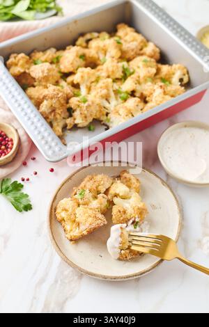 Draufsicht auf gebackenen Blumenkohl in einer Blechschale. Jede Blüte ist mit Brotkrumen beschichtet und mit geschmolzenem Käse und frischen Kräutern bestreut Stockfoto