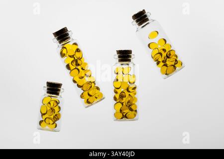 Transparente Glasflaschen gefüllt mit leuchtend gelben Omega-3- und Vitamin-D-Kapseln auf weißem Hintergrund. Stockfoto
