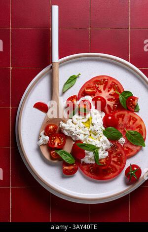Blick von oben auf einen wunderschön komponierten Caprese-Salat mit geschnittenen Reifen Tomaten, cremigem Burrata-Käse und frischen Basilikumblättern, fein gewürzt Stockfoto
