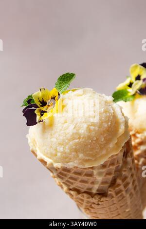 Eine Nahaufnahme eines Vanilleeises mit lebendigen essbaren Blüten und frischen Minzblättern, die eine entzückende und optisch ansprechende Leckerei schaffen. Stockfoto