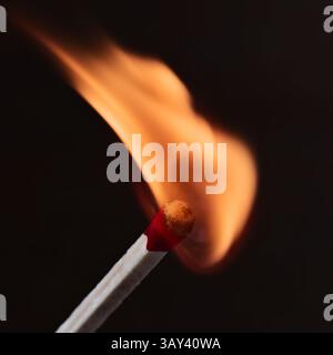 Eine Nahaufnahme, die einen Streichholzstab zeigt, der mit einer hellen orangen Flamme vor dunklem Hintergrund entzündet wird und die Lebendigkeit und Wärme des Feuers unterstreicht. Stockfoto