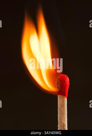 Ein Nahaufnahme-Foto eines Streichholzstifts, das eine leuchtende orangene Flamme vor dunklem Hintergrund erzeugt und das Wesen von Entzündung und Wärme einfängt. Stockfoto
