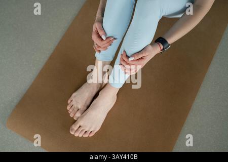 Eine Frau sitzt entspannt auf einer Yoga-Matte, die Hände liegen sanft auf den Beinen. Die Szene vermittelt ein Gefühl von Ruhe, Konzentration und Achtsamkeit in A Stockfoto