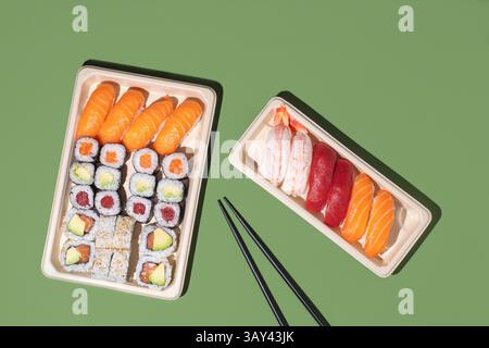 Minimalistischer Overhead-Sushi-Take-out-Boxen auf grünem Hintergrund mit Nigiri- und Maki-Rollen mit starker Richtungsbeleuchtung Stockfoto
