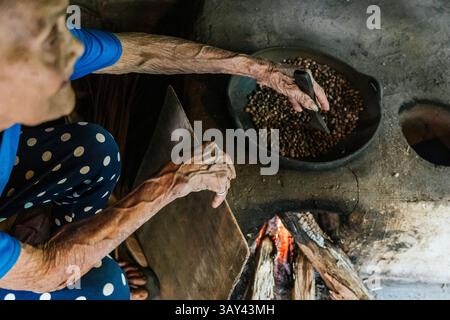 Eine ältere Frau röstet Kaffeebohnen über einer offenen Flamme und fängt dabei die Essenz traditioneller Methoden ein. In der Nahansicht werden die Hände hervorgehoben, die mit arbeiten Stockfoto